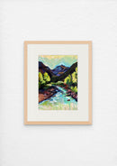 Framed painting of a mountain landscape with a river on a white wall