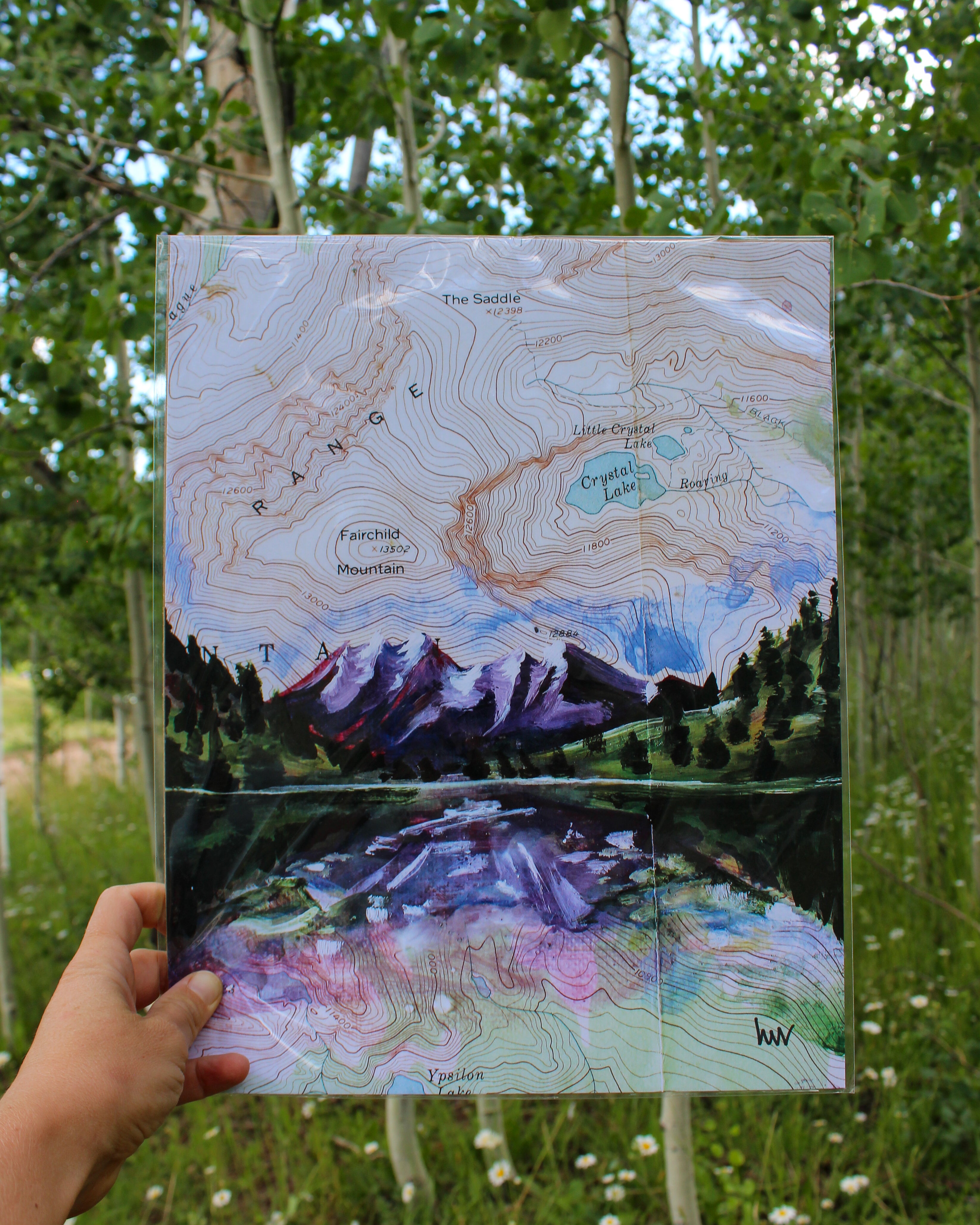Hand holding a map with a mountain landscape illustration against a natural background