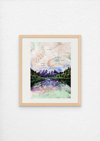 Framed artwork of a mountain landscape with a lake on a white wall
