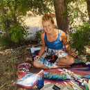 Woman sitting outdoors with a cat on a colorful blanket near a tree