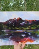 Artistic depiction of a mountain landscape held by a hand outdoors.