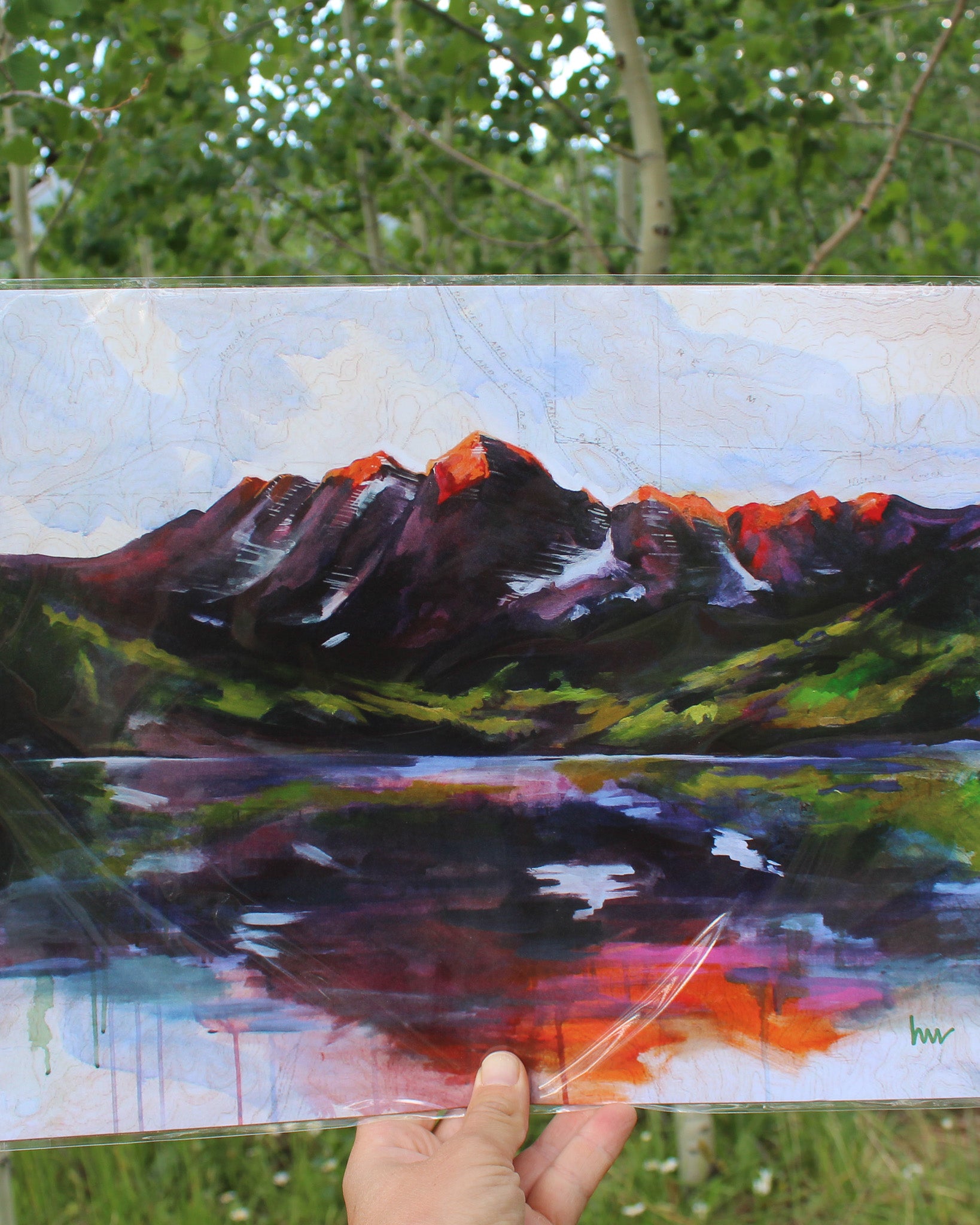 Artistic depiction of a mountain landscape held by a hand outdoors.