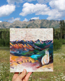 Painting of a mountain landscape with a mountain goat held in front of a real mountainous background.