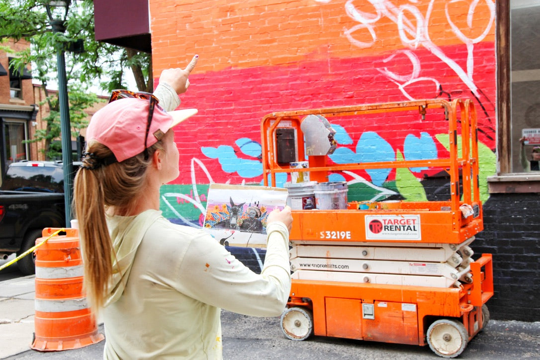 Person on a cherry picker painting a colorful mural on a building.