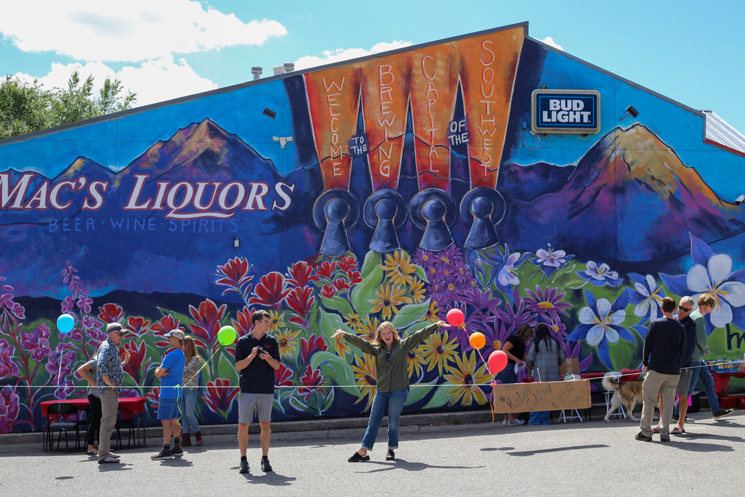 People posing in front of a colorful mural with 'Mac's Liquors' branding.