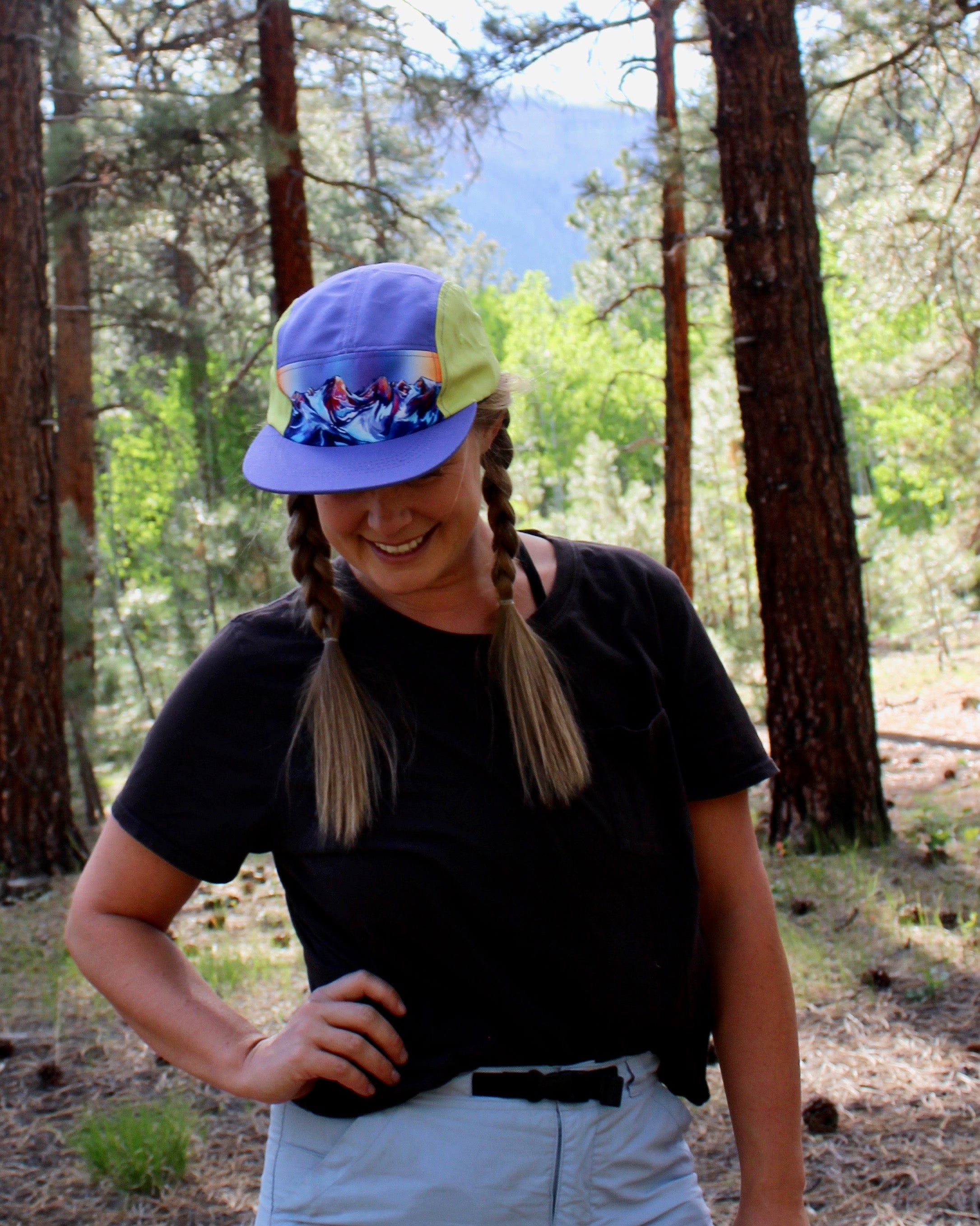 A woman wearing a colorful hat with a painting of a mountain range on it.