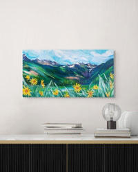 Painting of a mountain landscape with flowers on a wall above a desk.