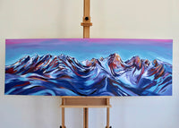 Painting of mountains on an easel against a white wall