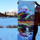Person holding a colorful mountain painting with a snowy landscape in the background