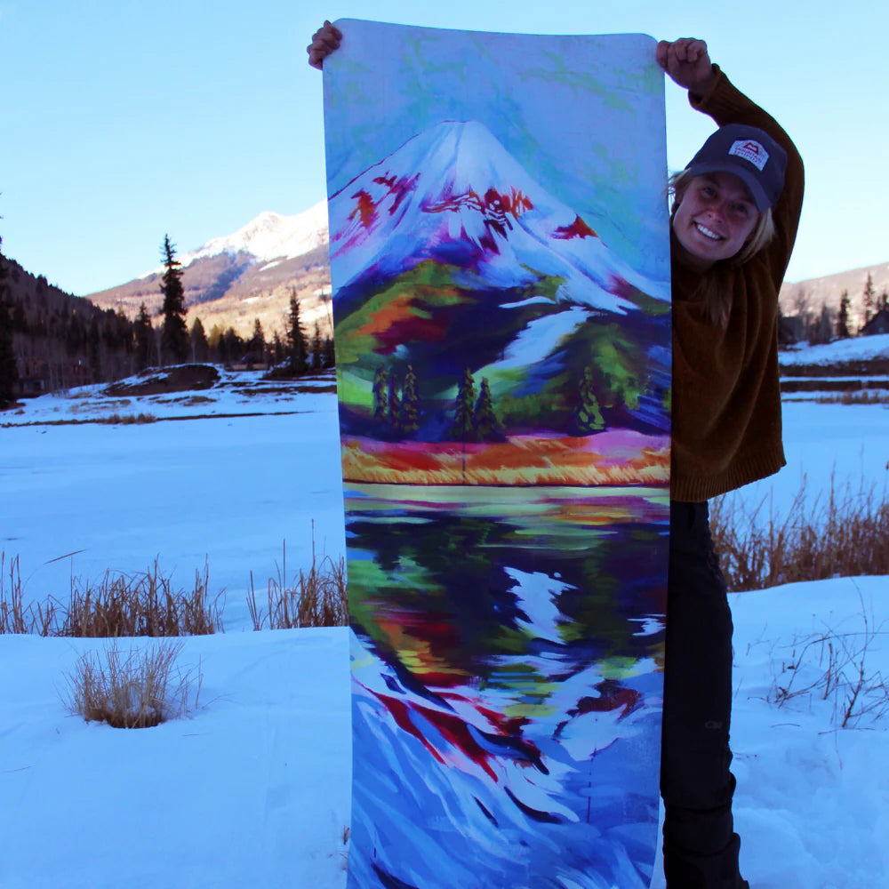 Person holding a colorful yoga mat with a mountain design in a snowy landscape