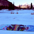 Colorful yoga mat on a snowy landscape with mountains and trees in the background